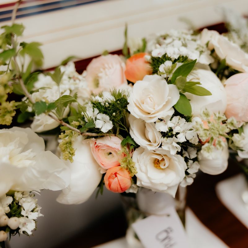 Bridal and bridesmaid bouquets in white, cream and peach with peonies and ranunculus resting on a mantel at a June wedding in Cedar Grove, Wisconsin